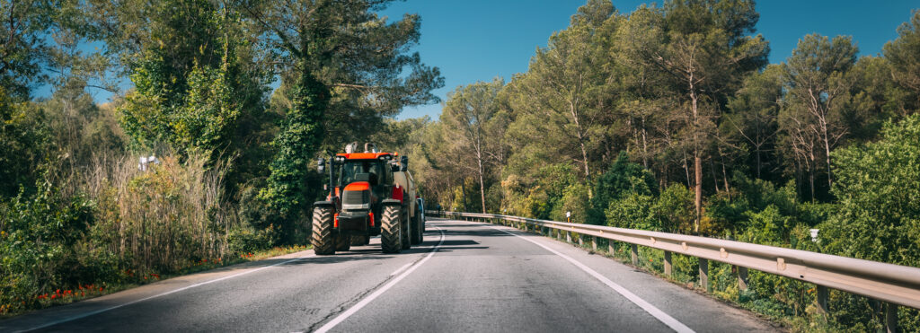 Tractor With Fertilizer Applicator With Tank In Motion On Country Road In Europe.